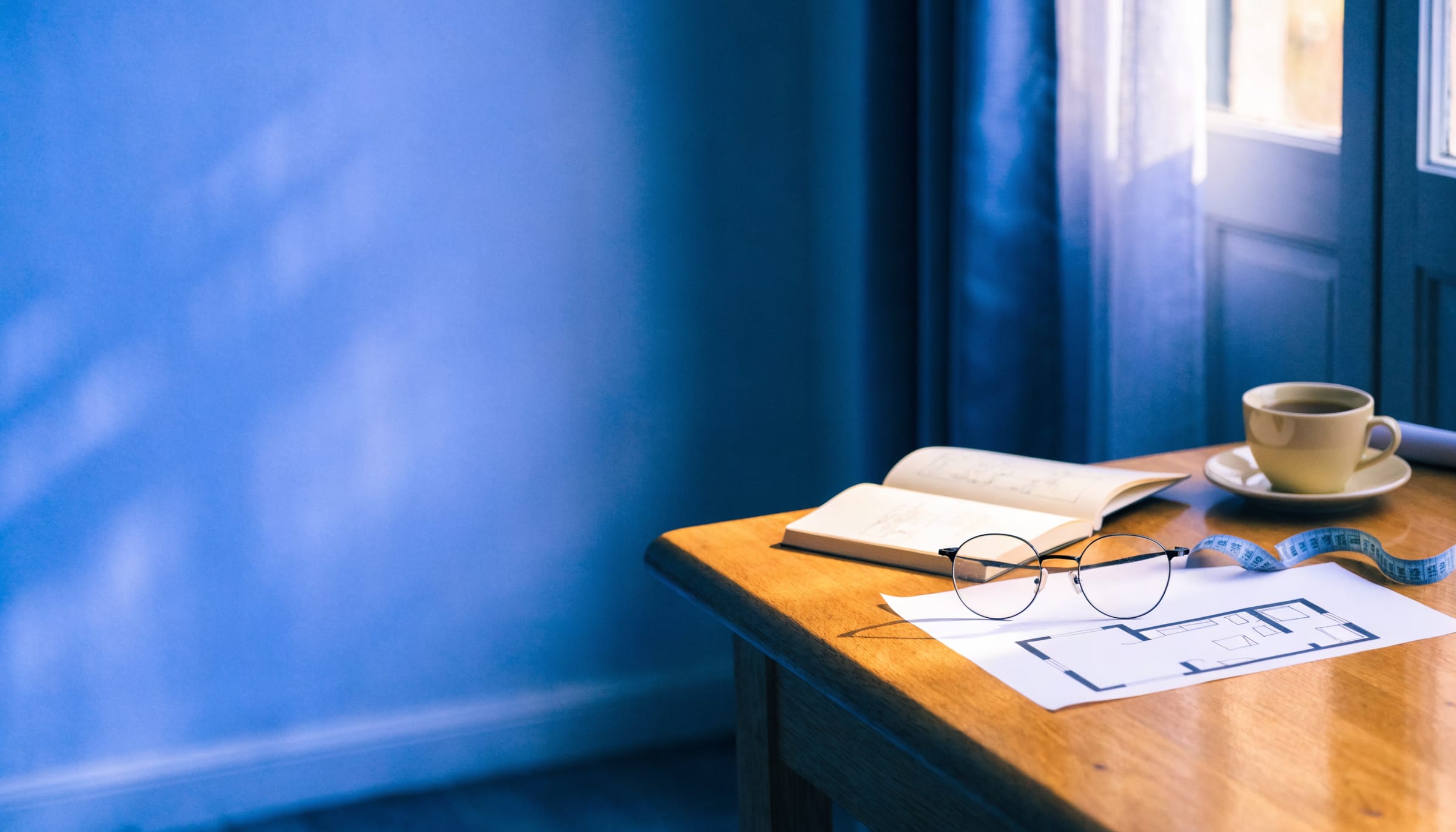 A planning table with a notebook, floor plan sketch, reading glasses and a cup of tea
