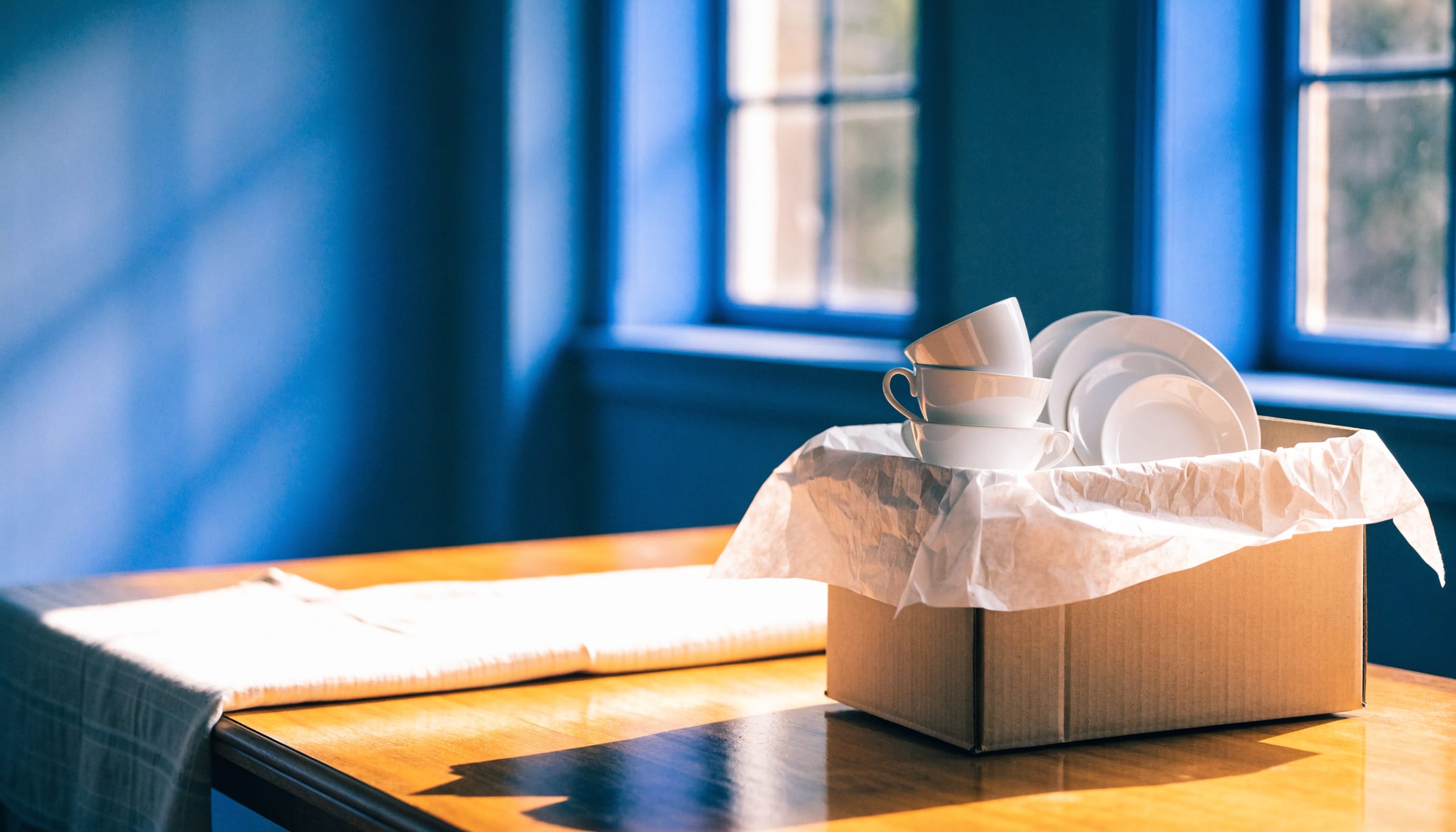 Plain white china being wrapped in paper and packed into a box on a dining table