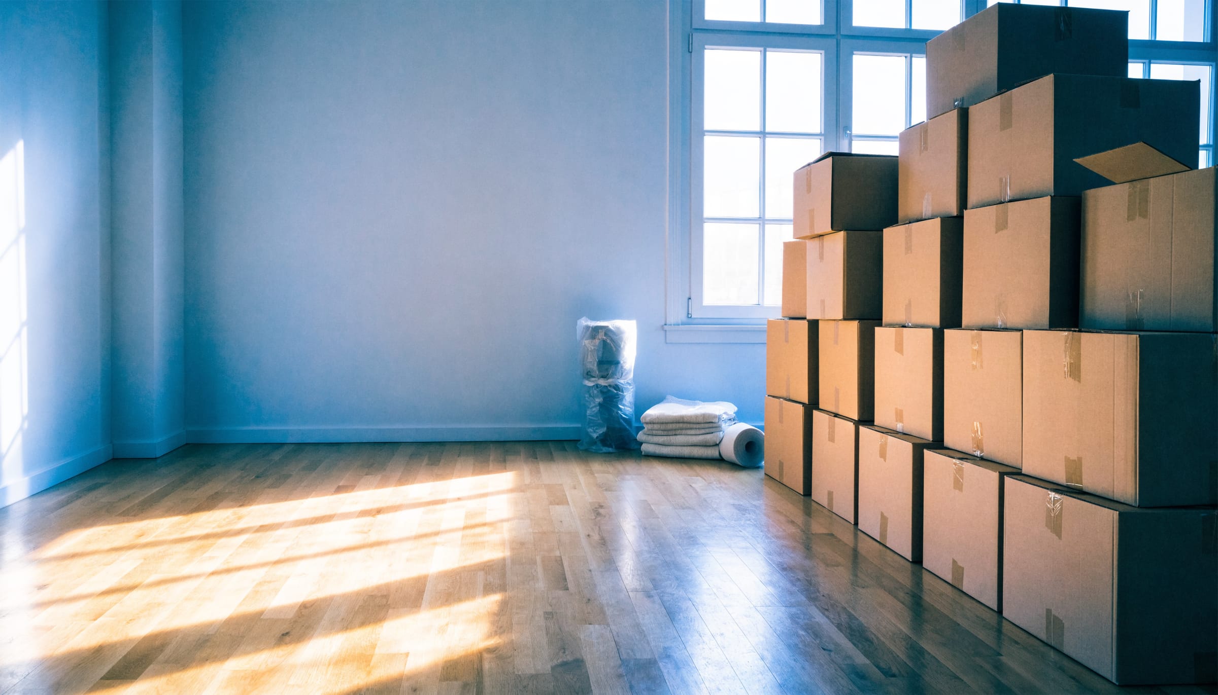 A tidy, sunlit room with neatly stacked moving boxes, folded linens and a roll of packing paper